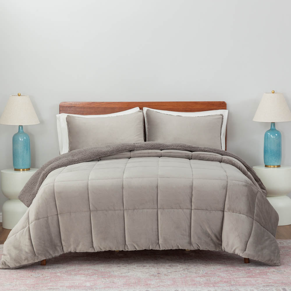 A gray quilted comforter draped over a bed with matching gray pillows and blue lamps on both sides.