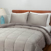 A gray quilted comforter draped over a bed with matching gray pillows and blue lamps on both sides.