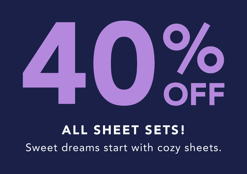 40% Off Sheet Sets – Sweet dreams start with cozy sheets. Image of a woman relaxing on a bed with plush purple sheets and pillows.