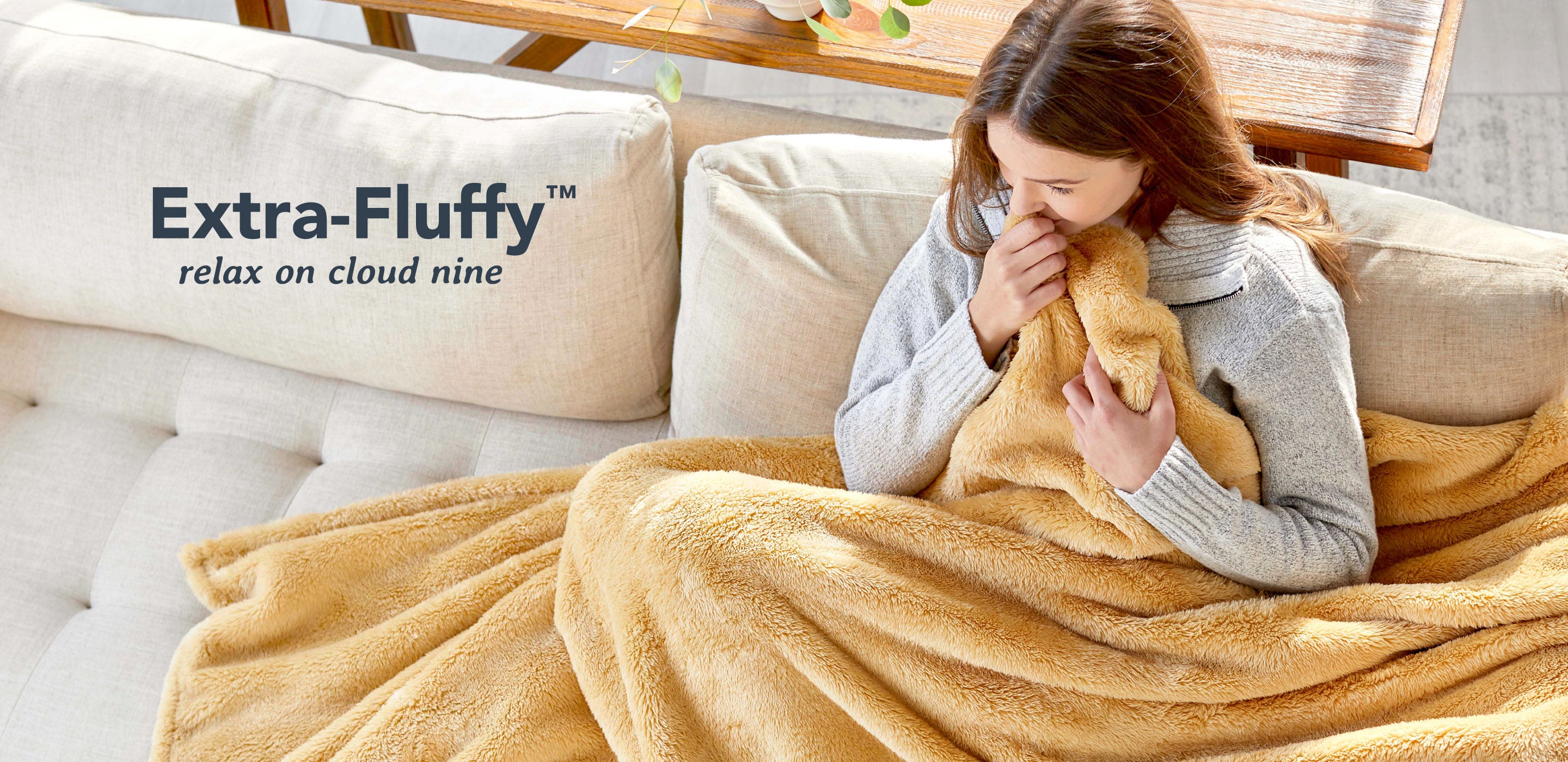 Image of a woman snuggling a yellow/orange Extra-Fluffy™ throw on her couch. text reads: Extra-Fluffy™ relax on cloud nice