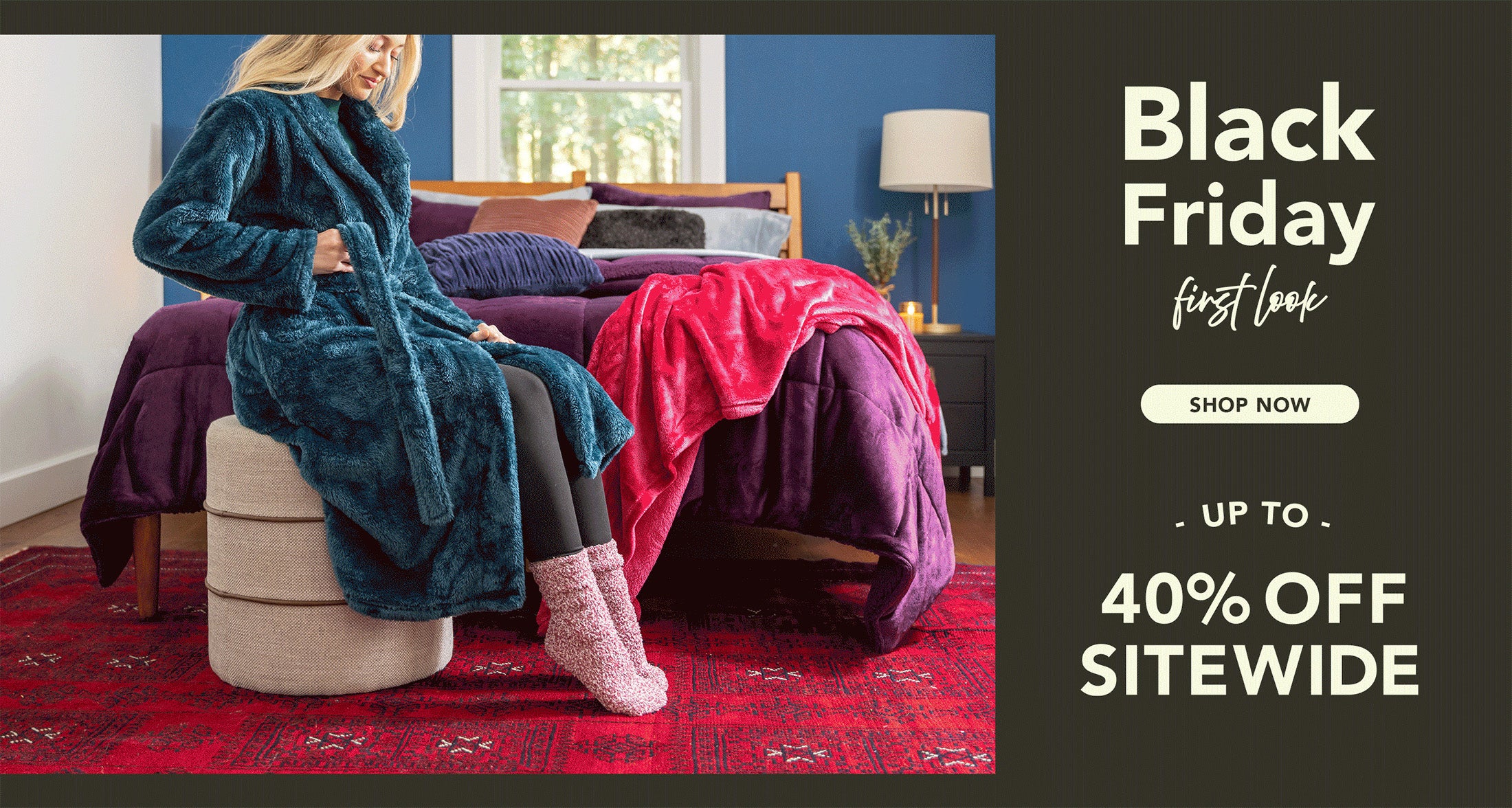 Black Friday First Look Shop Now Up to 40% OFF. Woman seated wearing robe in front of a bed