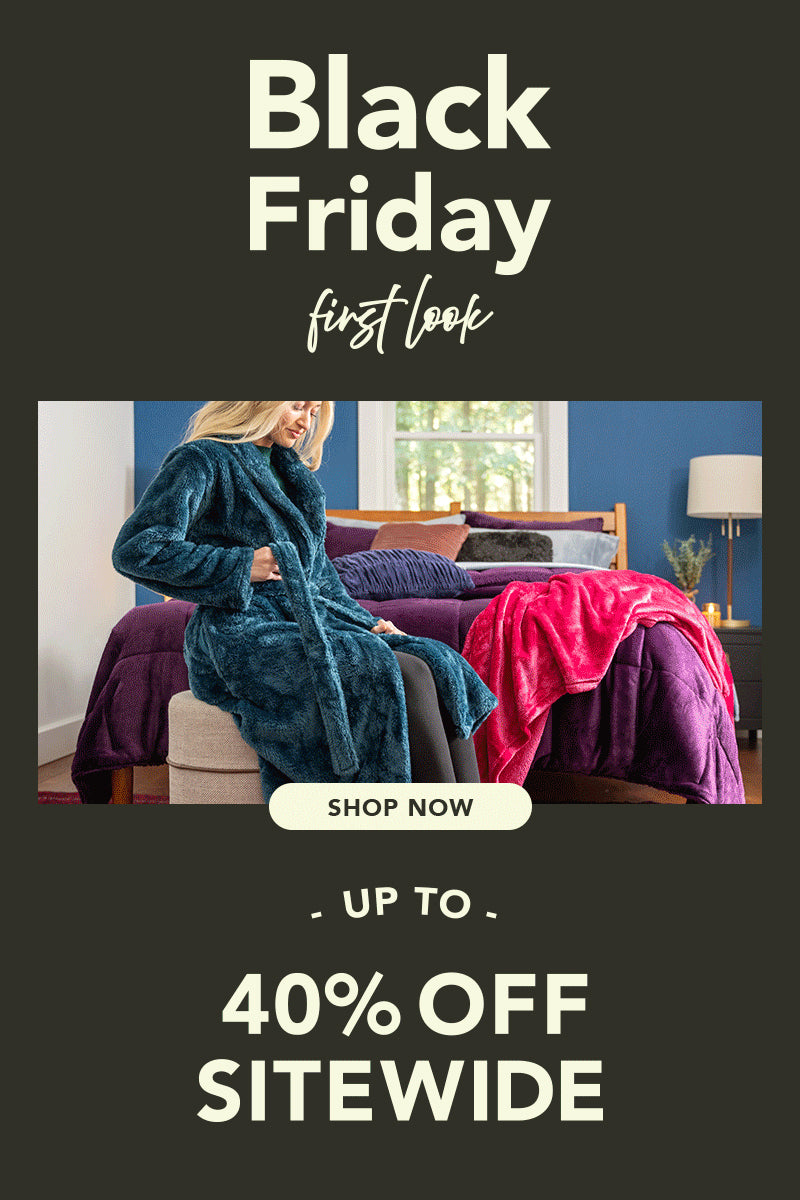 Black Friday First Look Shop Now Up to 40% OFF. Woman seated wearing robe in front of a bed