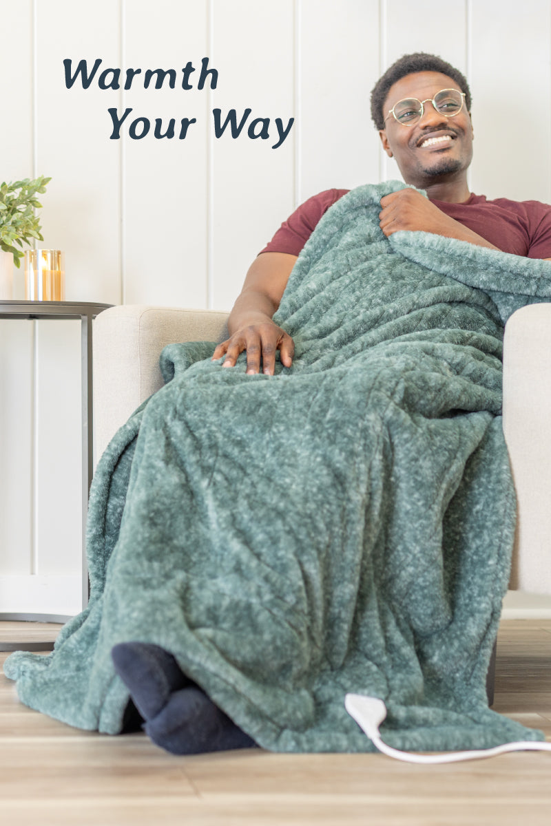 Image of a man sitting in a chair wearing a green heathered faux fur heated throw