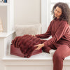 Woman in maroon outfit unfolding a red blanket on a white surface.