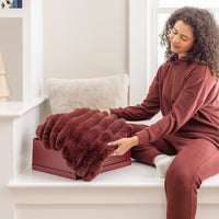 Woman in maroon outfit unfolding a red blanket on a white surface.
