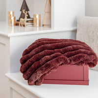 Folded burgundy blanket on a white surface with decorative items in the background