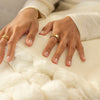 Close-up of hands wearing gold rings on a textured white surface