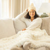 Woman sitting on a couch wrapped in a white blanket and wearing a matching hat.