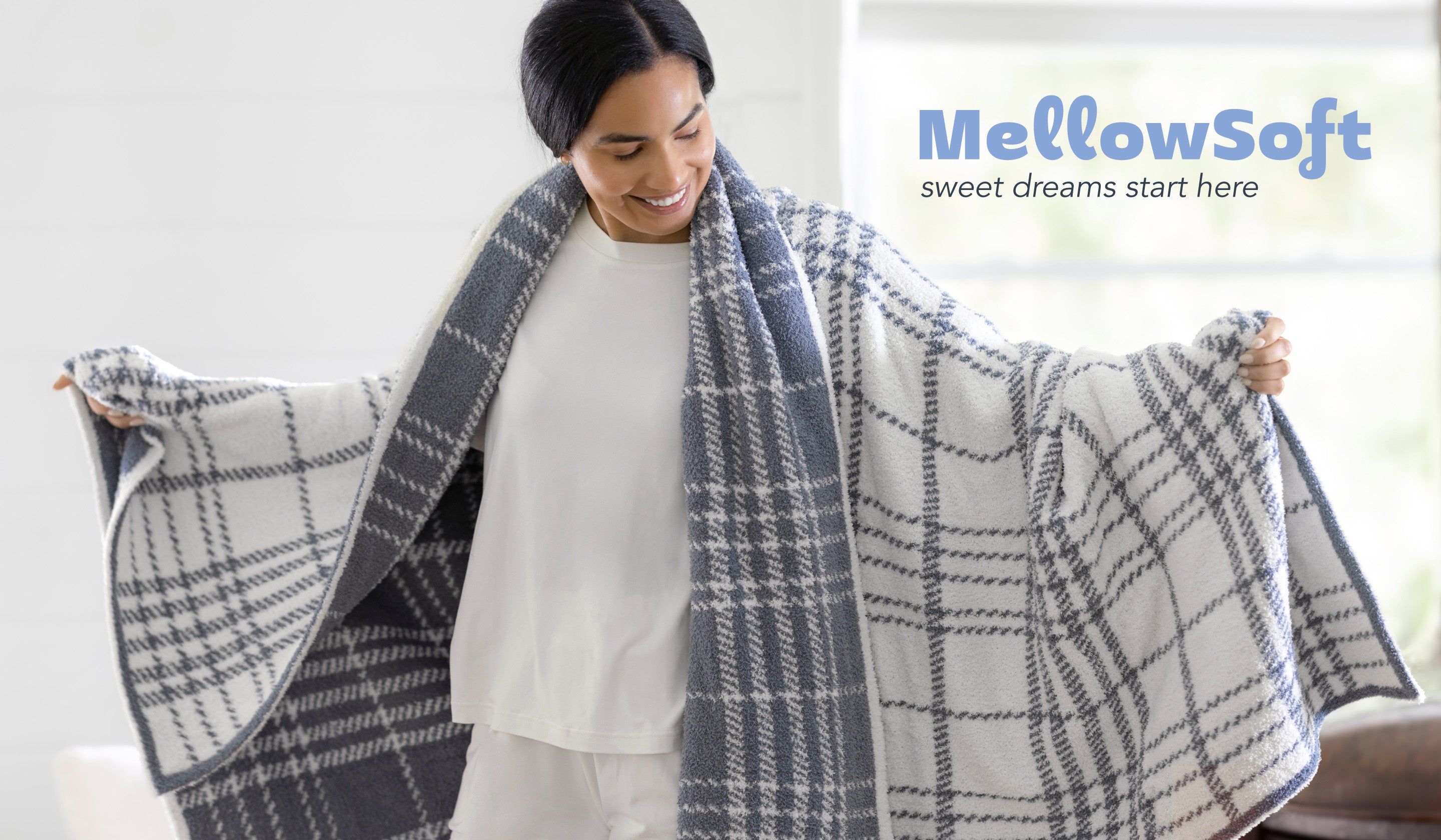MellowSoft - sweet dreams start here. image of a woman wearing a plaid blue and white throw sound her shoulders with her arms spread open to show how stretchy and luxe MellowSoft is. 