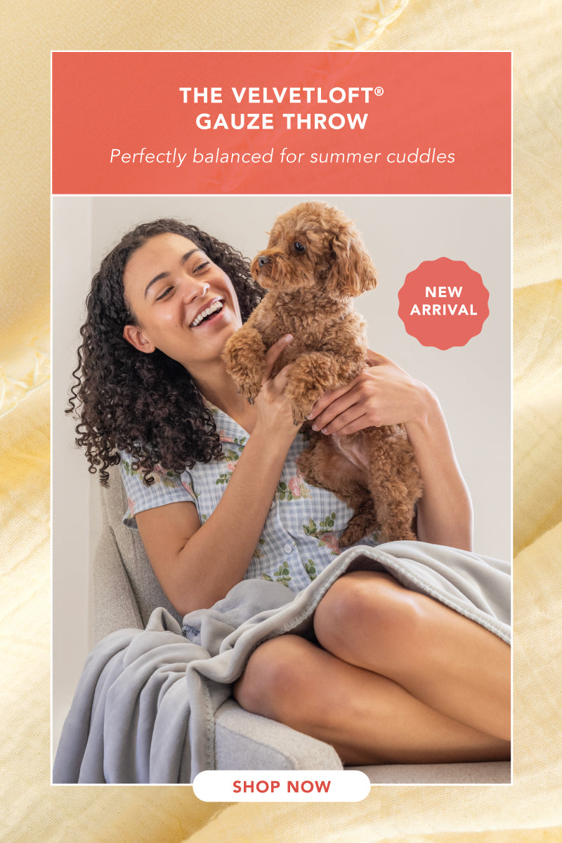 New Arrival! The VelvetLoft® Gauze Throw. Perfectly balanced for summer cuddles. Shop Now. Image of a woman and her poodle enjoying a soft blanket on a corner chair.