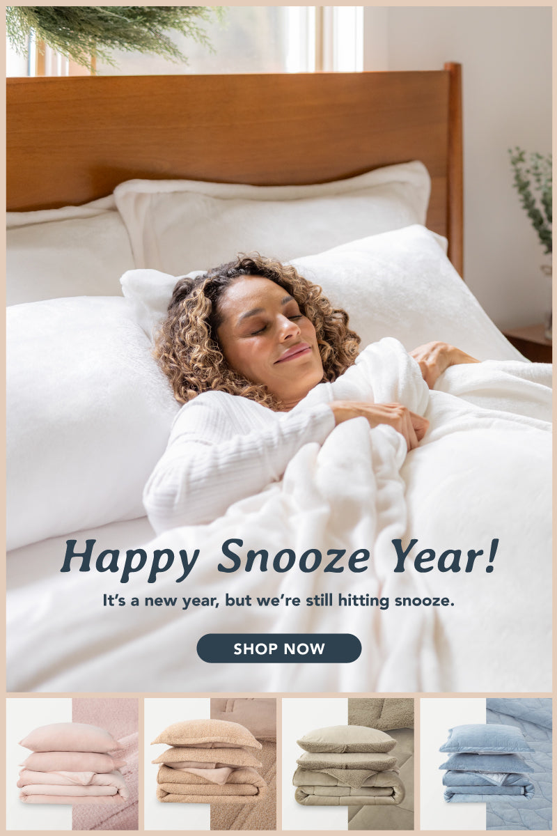 Collage of cozy bedding and blankets in various soft colors, including blush pink, light blue, beige, and cream. A smiling woman relaxes in bed, wrapped in plush white bedding, with text reading 'Happy Snooze Year! It’s a new year, but we’re still hitting snooze.' The image highlights comfort and warmth with a call-to-action button that says 'Shop Now.'